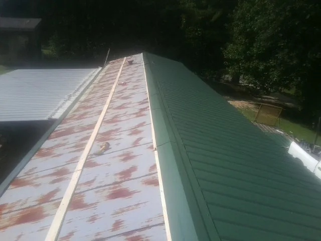 Old rusted panels beside newly installed green metal roofing — Wind Damage Roof Repair by Roofing Brothers in Saint Albans