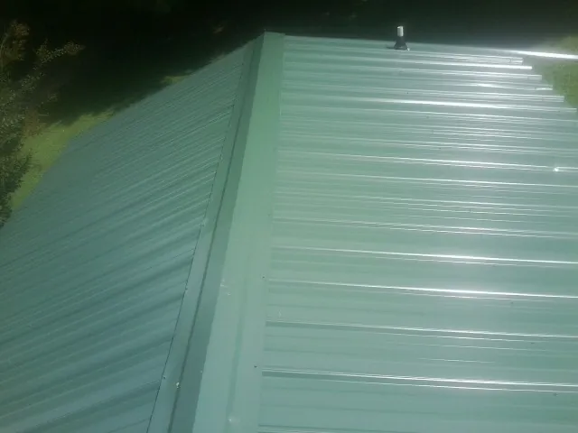 New green metal panels meeting at the ridge of a roof — Flat Roof Repair work by our crew in Saint Albans