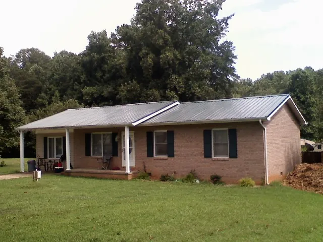 Gray metal roof on a brick ranch house with a side carport in Saint Albans