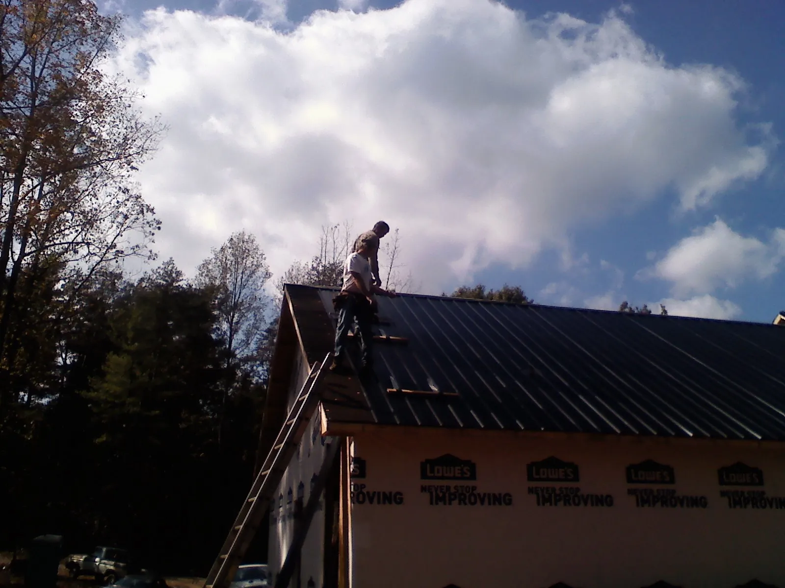 Roofer fastening dark metal panels high against a cloudy sky, from a Roof Inspection job in Saint Albans